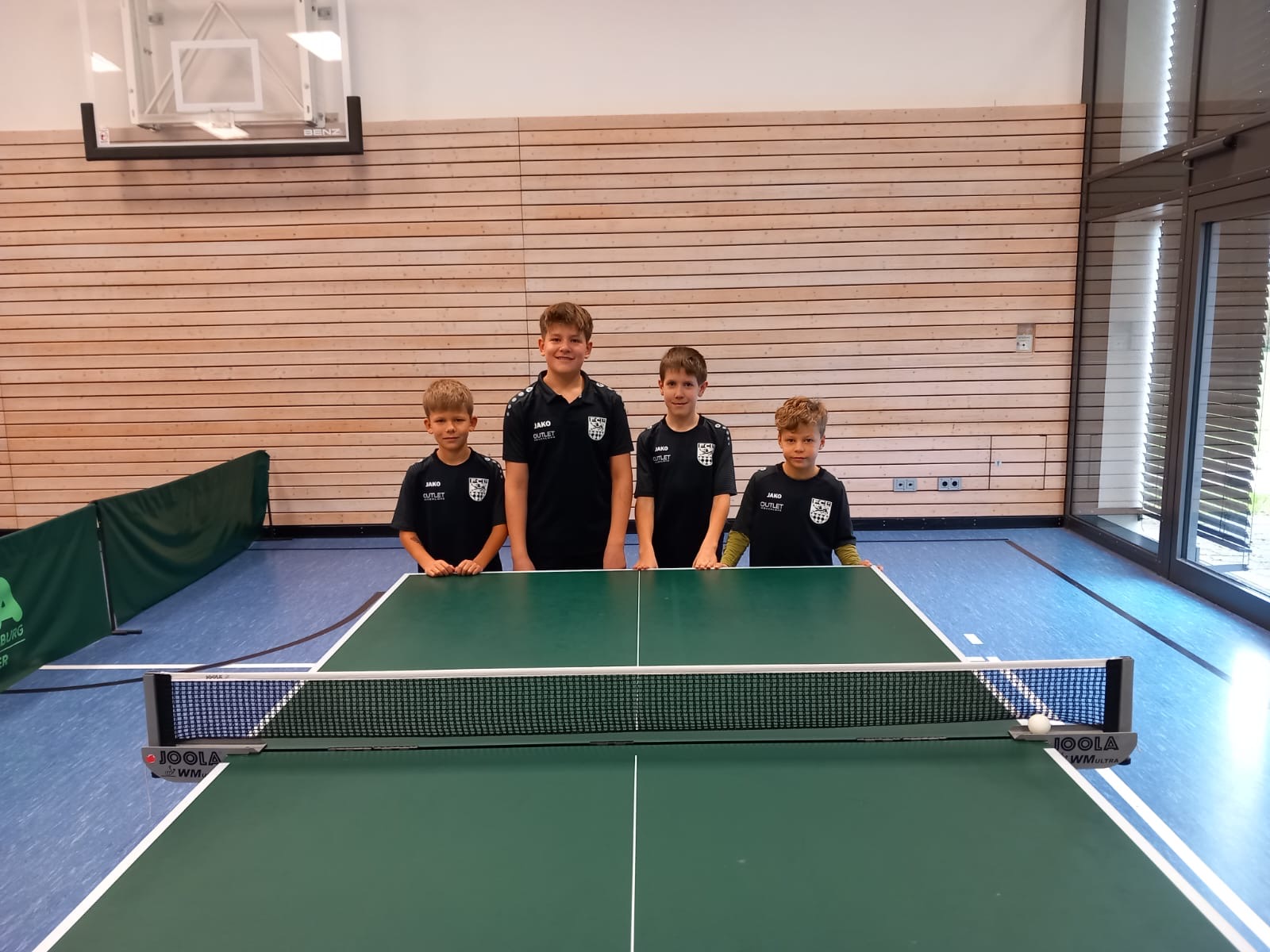 Auf dem Bild sind 4 Jungs vor einer Tischtennisplatte zu sehen. Von links nach rechts stehen Jaron Baumann, Benjamin Ehrmann, Marcel Jäger und Jannis Trump 